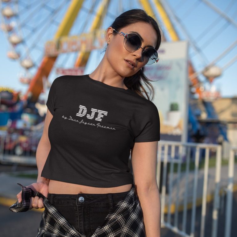 Frau mit Sonnenbrille trägt ein schwarzes DJF by Dean Jayson Freeman T-Shirt vor einem Rummelplatz.