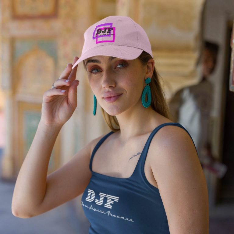 Junge Frau mit pinker DJF by Dean Jayson Freeman Kappe und blauen Ohrringen, lächelt und posiert in einem historischen Gebäude.