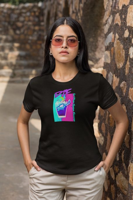 Junge Frau in schwarzem DJF by Dean Jayson Freeman T-Shirt mit buntem Cocktail Design und Sonnenbrille, vor einer Steinmauer.