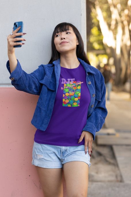 Frau mit Smartphone, trägt lila DJF by Dean Jayson Freeman T-Shirt und Jeansjacke, posiert draußen.