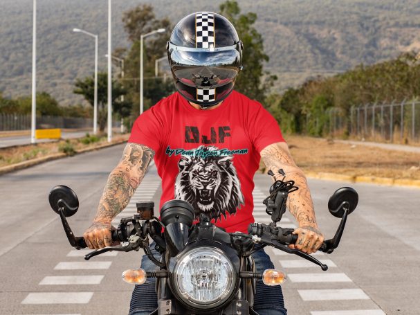 Mann auf Motorrad in rotem DJF by Dean Jayson Freeman T-Shirt mit Löwenmotiv, trägt einen Helm mit Schachbrettmuster.