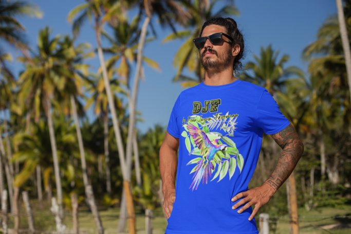 Mann in blauem DJF by Dean Jayson Freeman T-Shirt mit Motiv, steht vor Palmen und Sonnenschein.